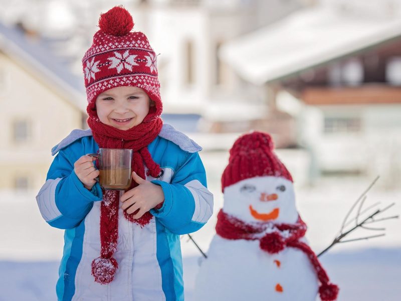 dieťa so šálkou kakaa v ruke v zime pred snehuliakom